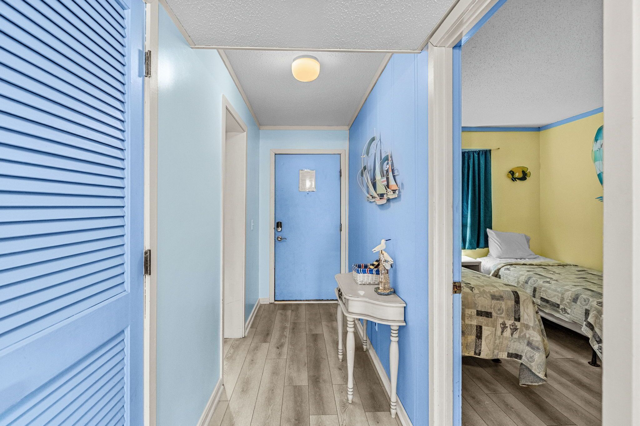 Ein Flur, der in ein Schlafzimmer mit einem Bett, einem Nachttisch und einer Wandlampe führt.