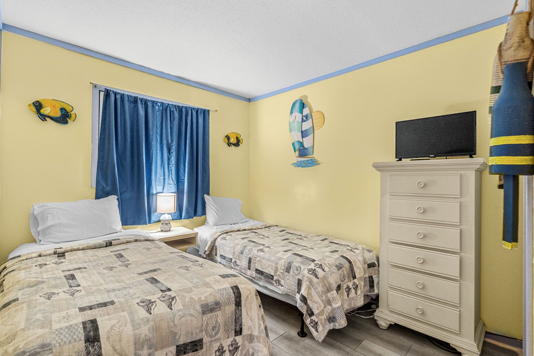 Una habitación con dos camas, un aparador, un televisor y decoración de peces en la pared.