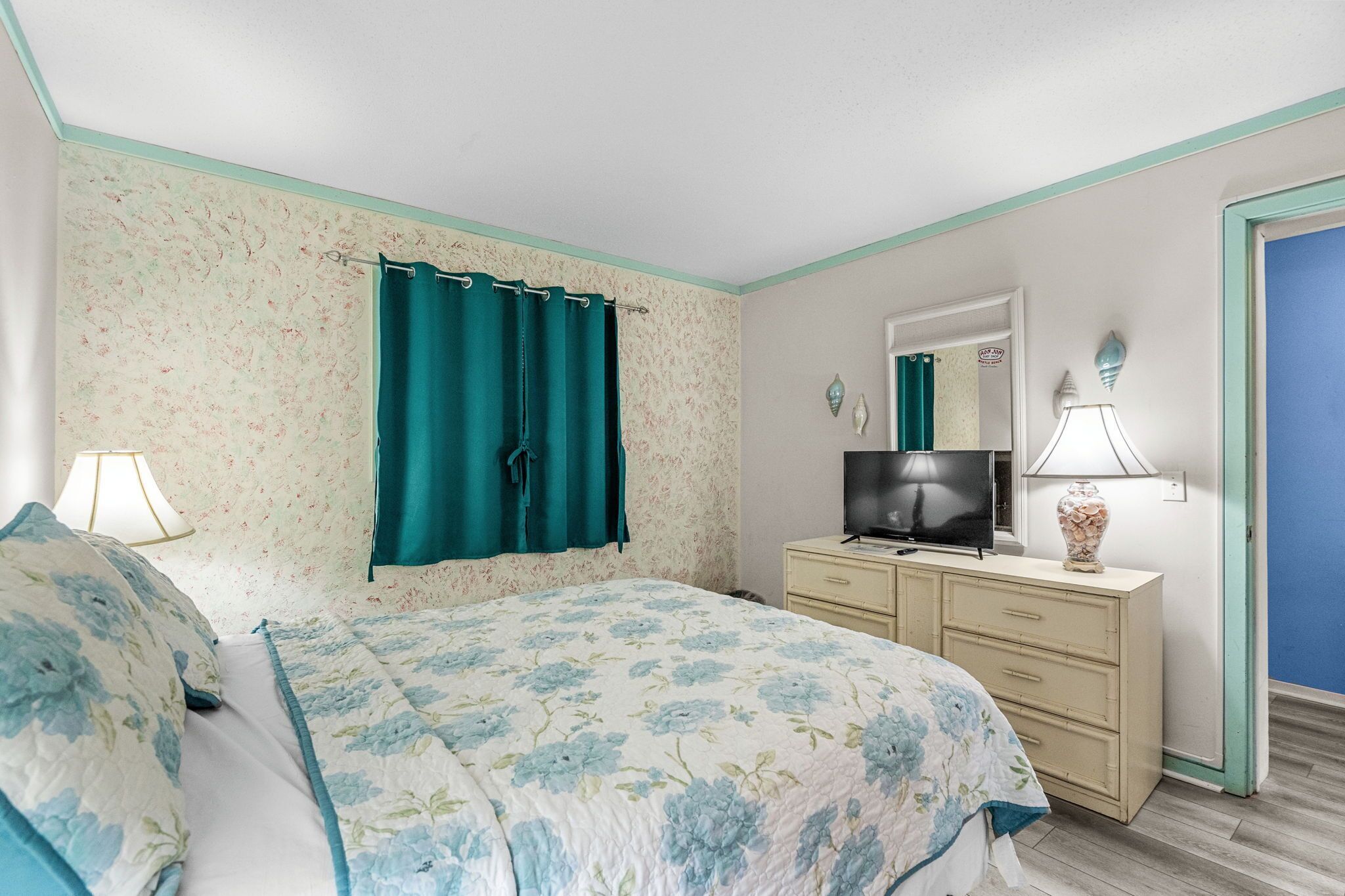 A bedroom with a floral bedspread, a television on a dresser, and a mirror above the dresser.