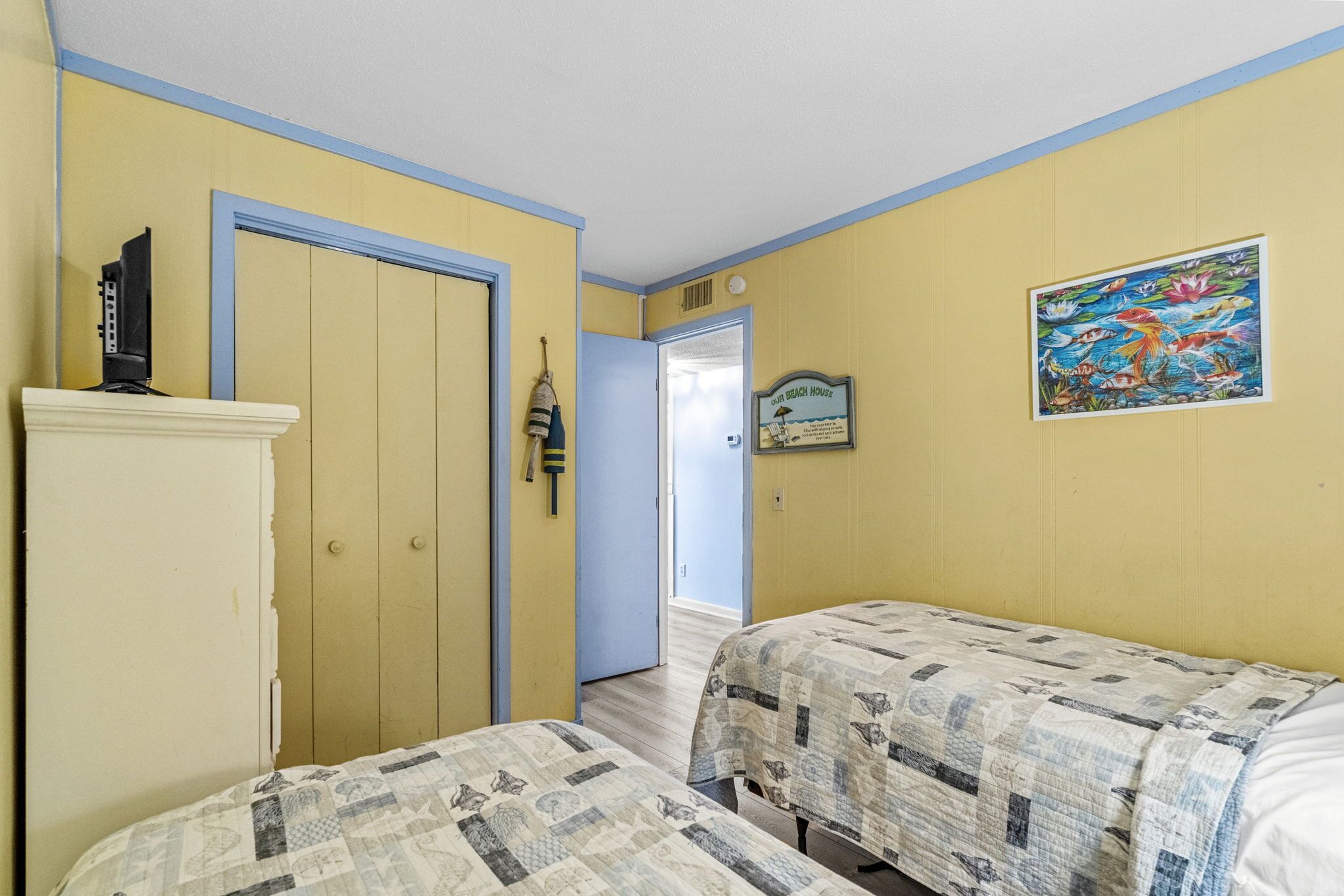 Una habitación con dos camas, una puerta, un televisor sobre un mueble y un cuadro en la pared.