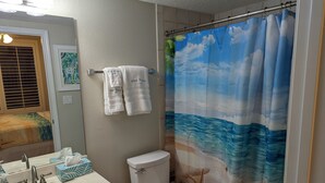 A bathroom with a toilet, sink, and shower curtain depicting a beach scene. - Breathtaking views directly facing the Gulf!  3bd/3bath/6 (Fort Walton Beach)
