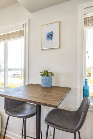 A dining area with a wooden table, two chairs, a potted plant, and a framed artwork on the wall. - Best View and Amenities on the Island. Stay & Play (Wrightsville Beach)