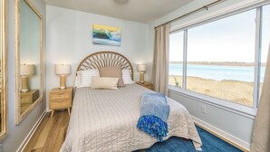 A bedroom with a large window, a bed with a headboard, bedside tables, and a mirror.