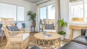 A spacious living area with wicker furniture, a round table, and large windows offering a view of the city.