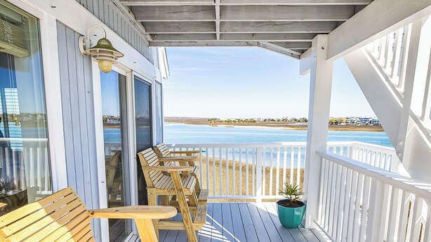 A wooden deck with a railing, wooden chairs, and a table.