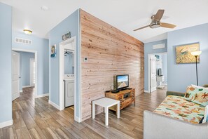 A living room with a wooden accent wall, a ceiling fan, a television, and a sofa with a floral cushion.