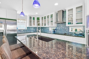 Una cocina moderna con armarios blancos, un refrigerador de acero inoxidable, salpicadero de azulejos azules y encimera de granito.