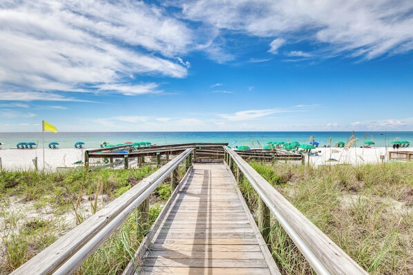 A wooden boardwalk leading to a beach with umbrellas and beach chairs.
