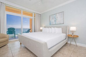 A hotel room with a large bed, a chair, a nightstand, and a view of the ocean.