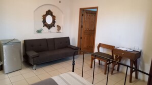 Una habitación con un sofá, una silla de madera, una mesita y una puerta.