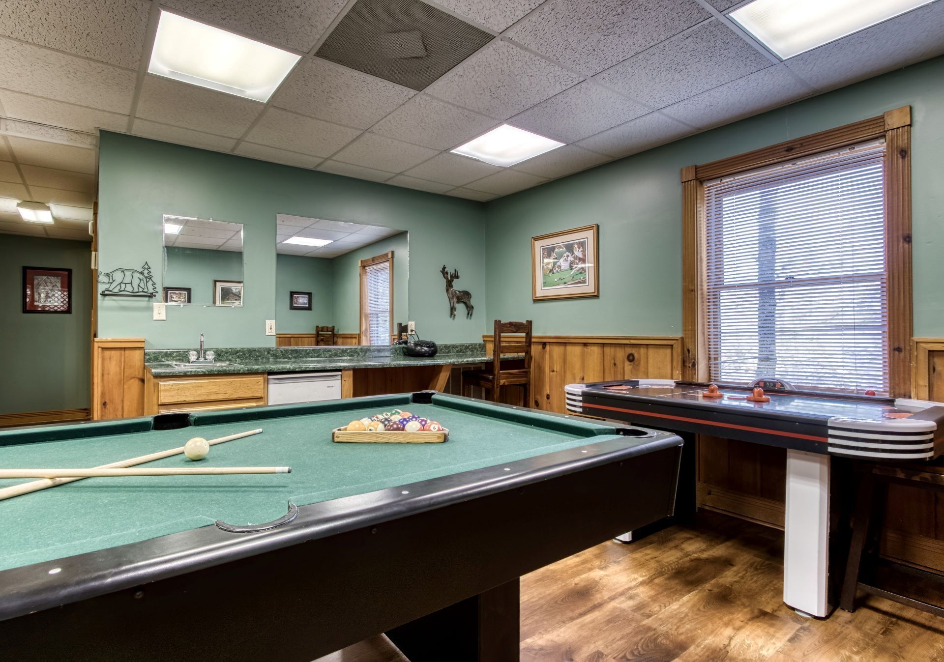 A pool table with a green felt surface, wooden cabinets, and a mirror above it.