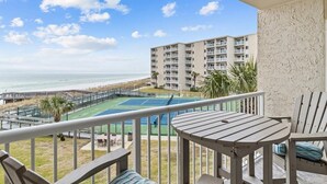 A balcony with a view of a tennis court and beach, furnished with a table and chairs. - 321- Amazing Unit with Gorgeous View of the Gulf & Free Beach Service (Destin)