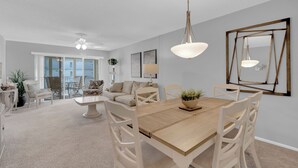 Un vaste espace dédié à la salle à manger, avec une table en bois, des chaises blanches et des luminaires suspendus.