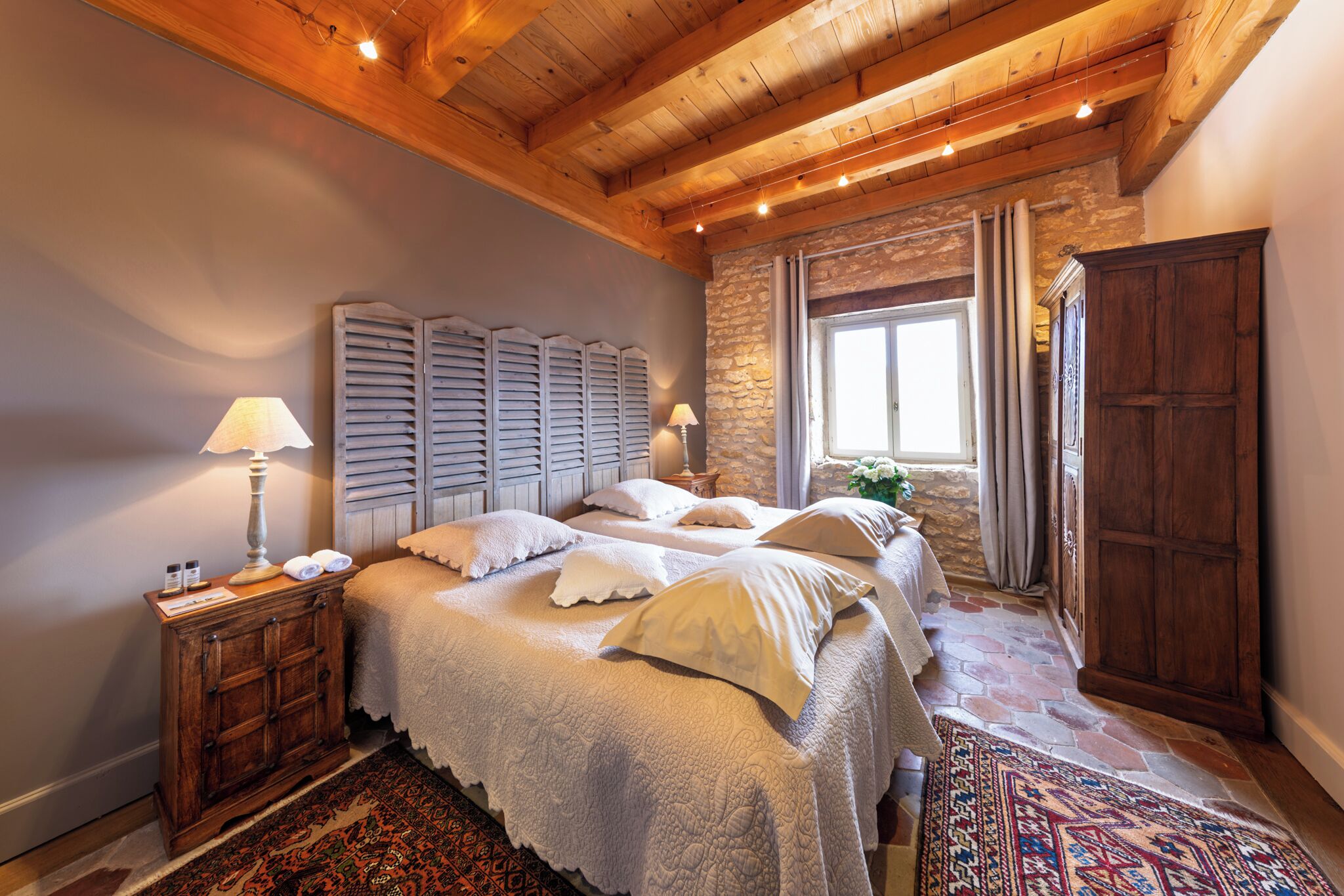 A bedroom with a large bed, wooden headboard, stone wall, and a wooden wardrobe.