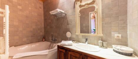 A bathroom with a bathtub, a sink, a vanity with cabinets, a mirror, and a towel rack.