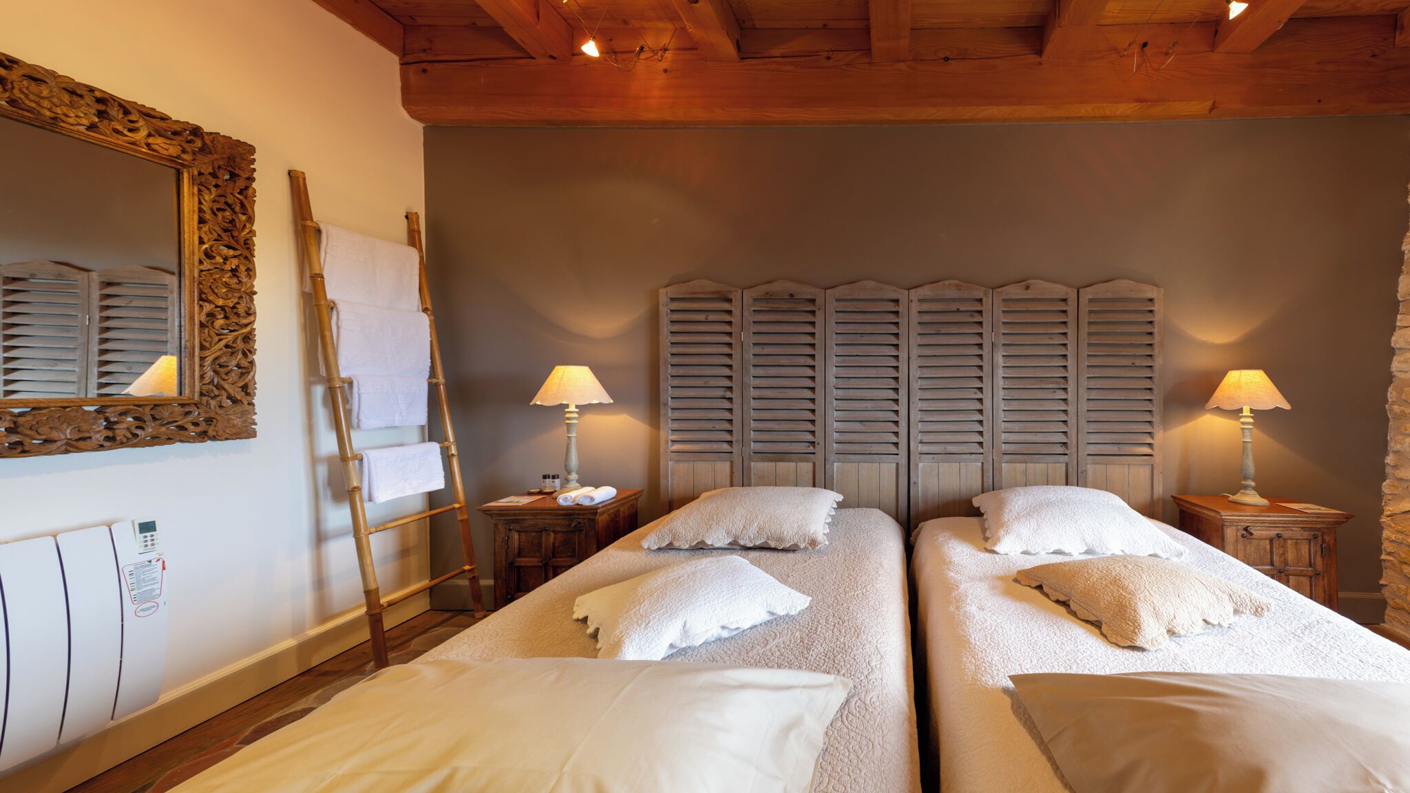 Una habitación con dos camas, cabeceros de madera, una escalera, un espejo y lámparas de noche.