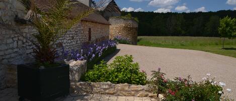 Ein Steinhaus mit Strohdach, umgeben von einem Schotterweg und Blumenbeeten.