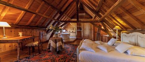 Un dormitorio acogedor en el ático, con techo de madera, una cama grande, una mesita pequeña, una silla y una alfombra decorativa.