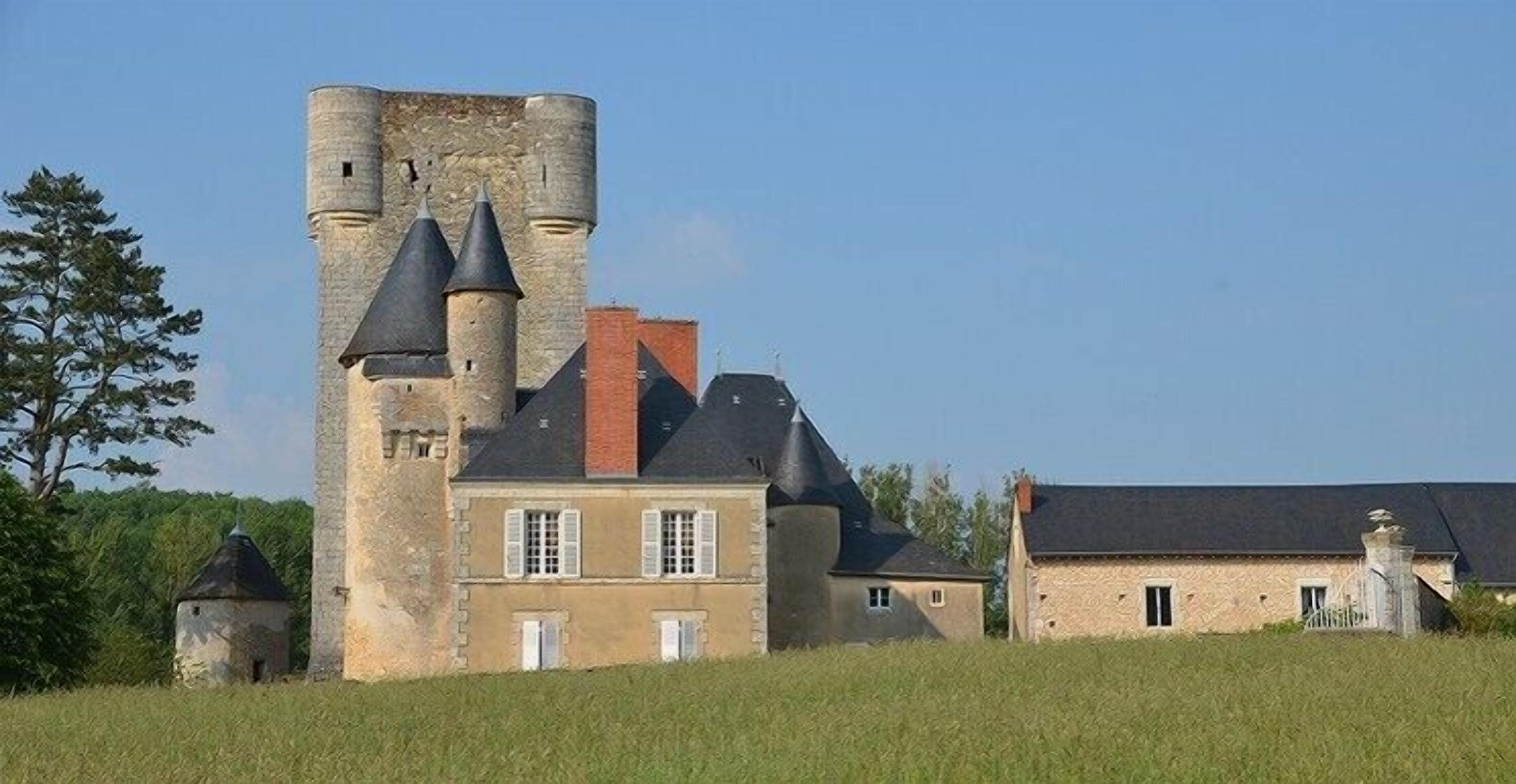A historic stone building with a prominent tower and multiple conical roofs, surrounded by a grassy field and trees.