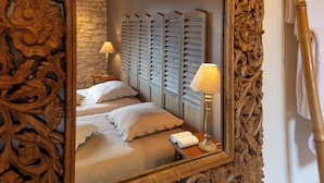 Un dormitorio con un espejo grande que refleja una cama con dos almohadas y una lámpara en una mesita de noche.
