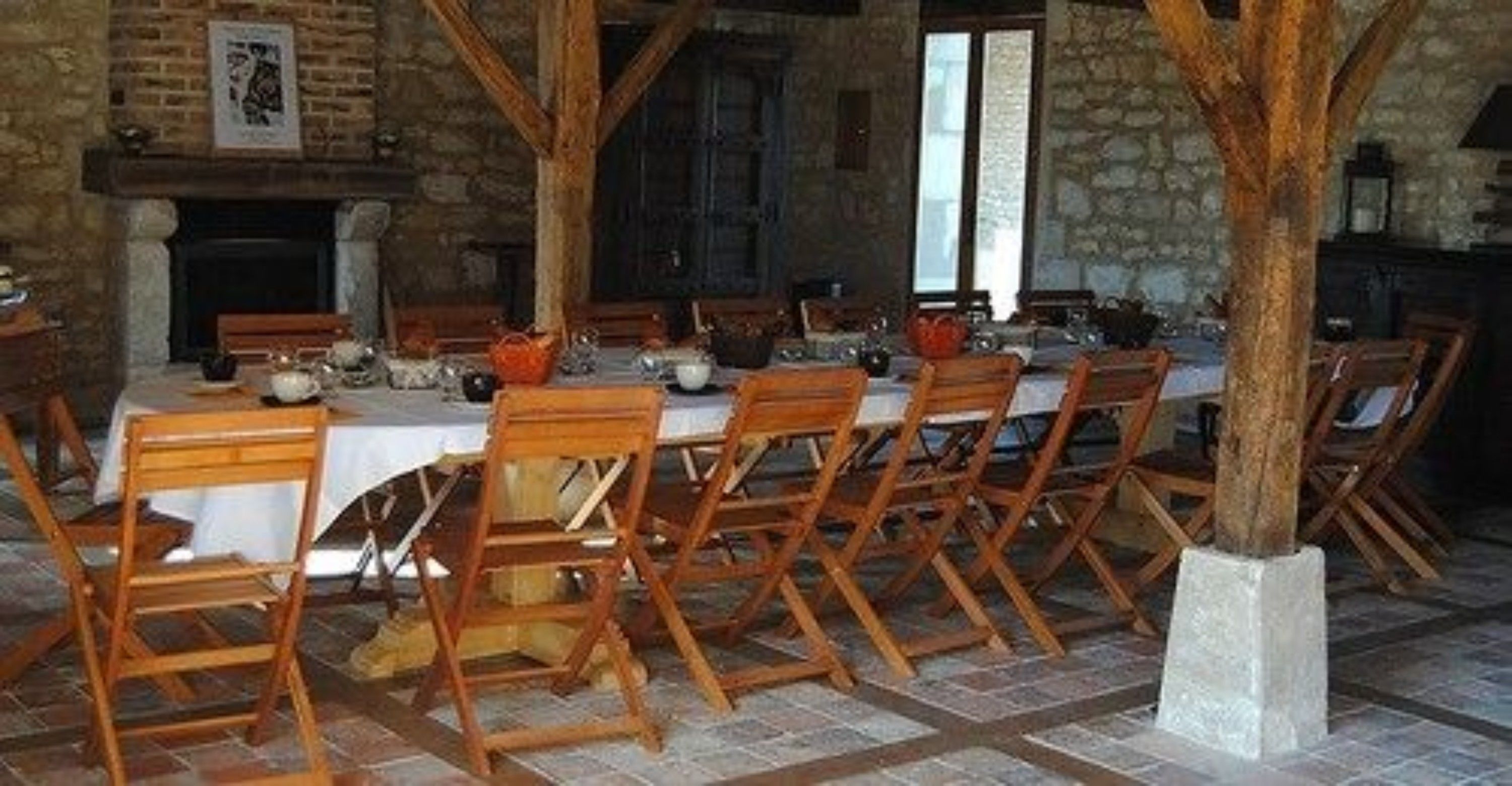 Un comedor con una mesa larga dispuesta para una comida, sillas de madera y una pared de piedra al fondo.