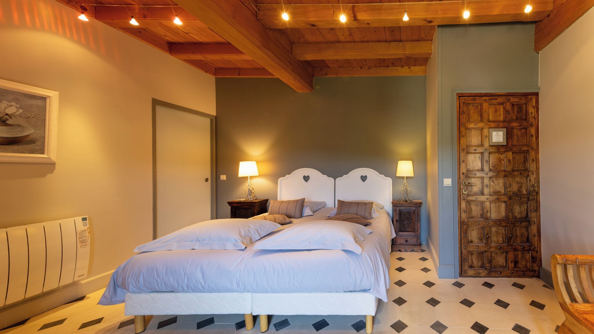 Een slaapkamer met een groot bed, twee nachtkastjes met lampen, een houten deur en een radiator.