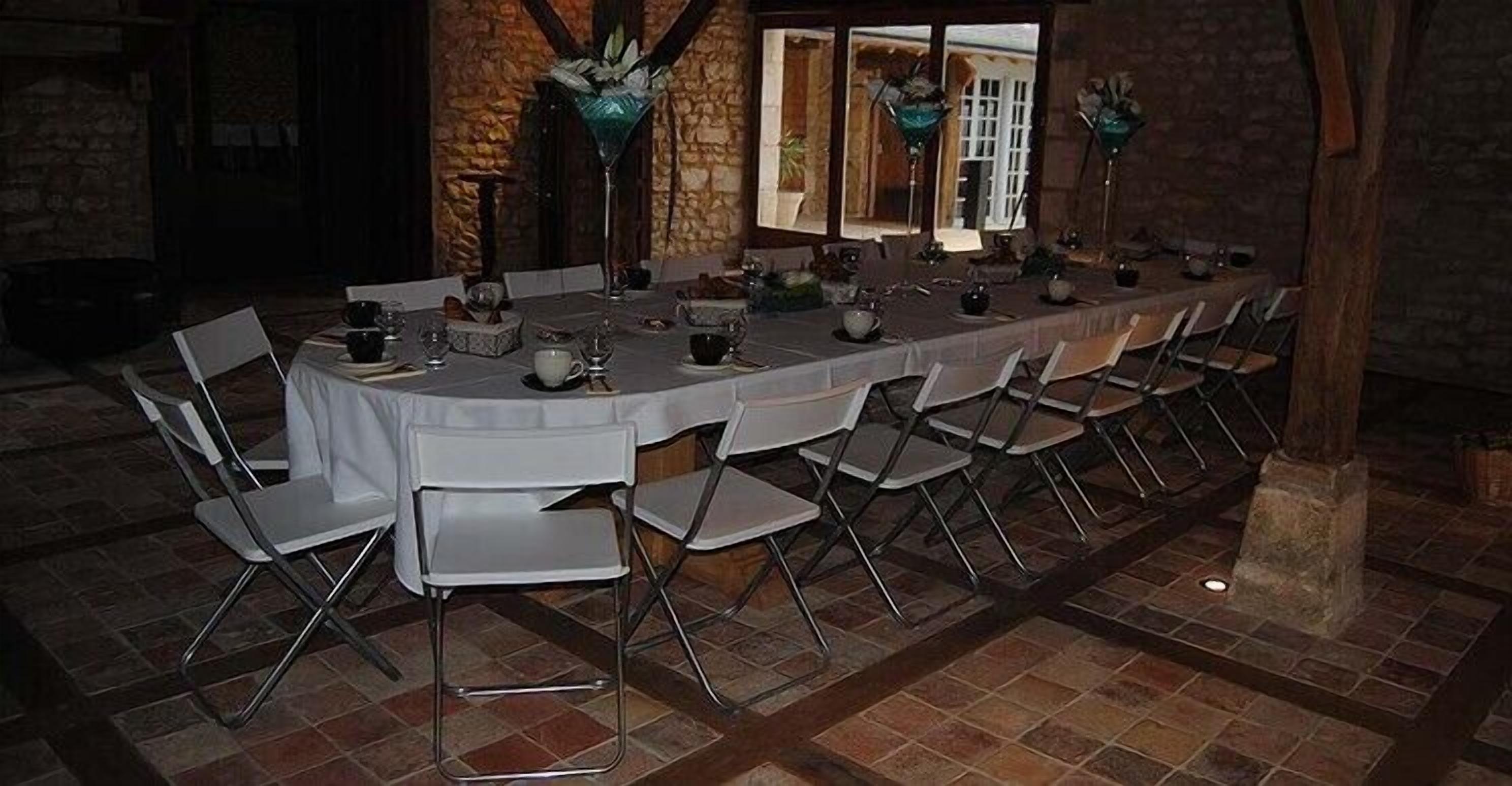 A long dining table set with chairs, surrounded by stone walls and a window with curtains.