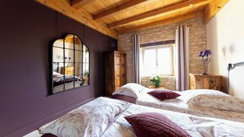 Un dormitorio con dos camas, vigas de madera, paredes de piedra, un espejo y una ventana con cortinas.