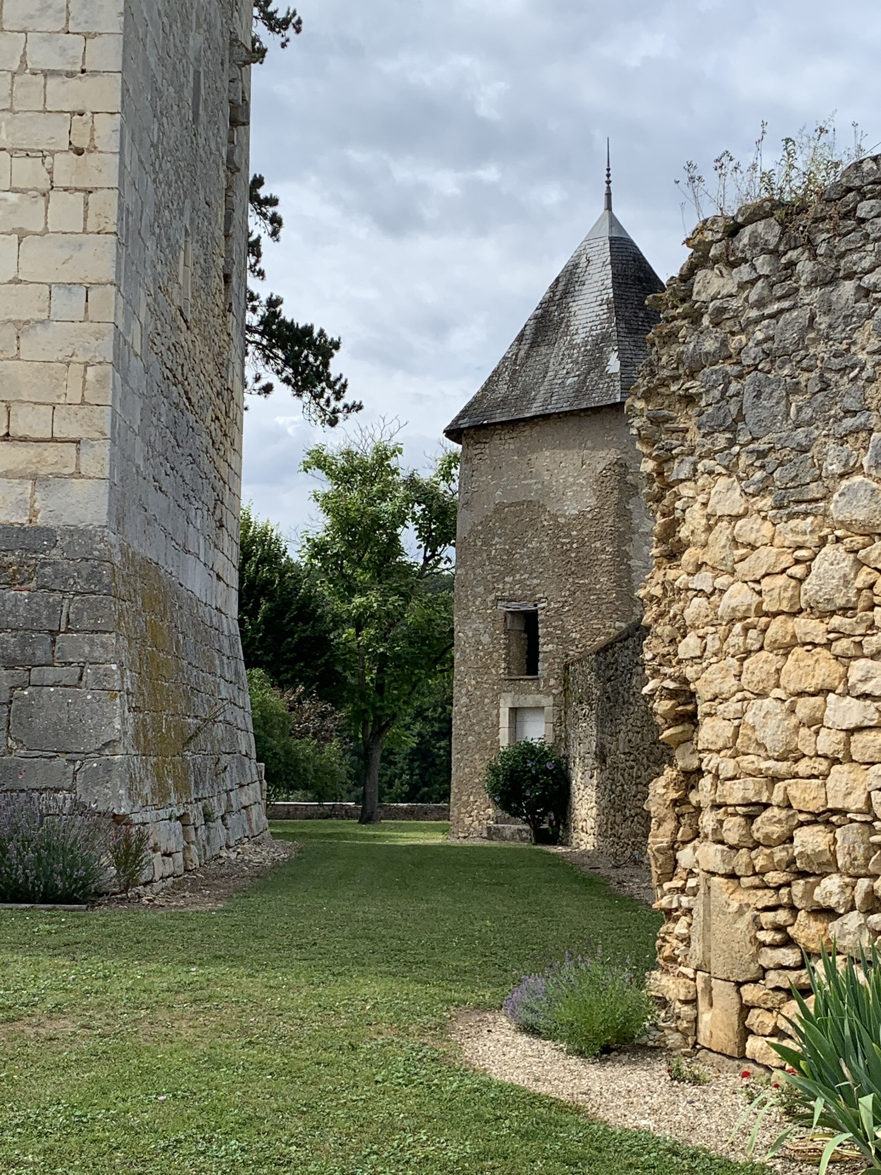 Un bâtiment en pierre doté d’une tour, entouré d’une zone herbeuse et d’arbres.