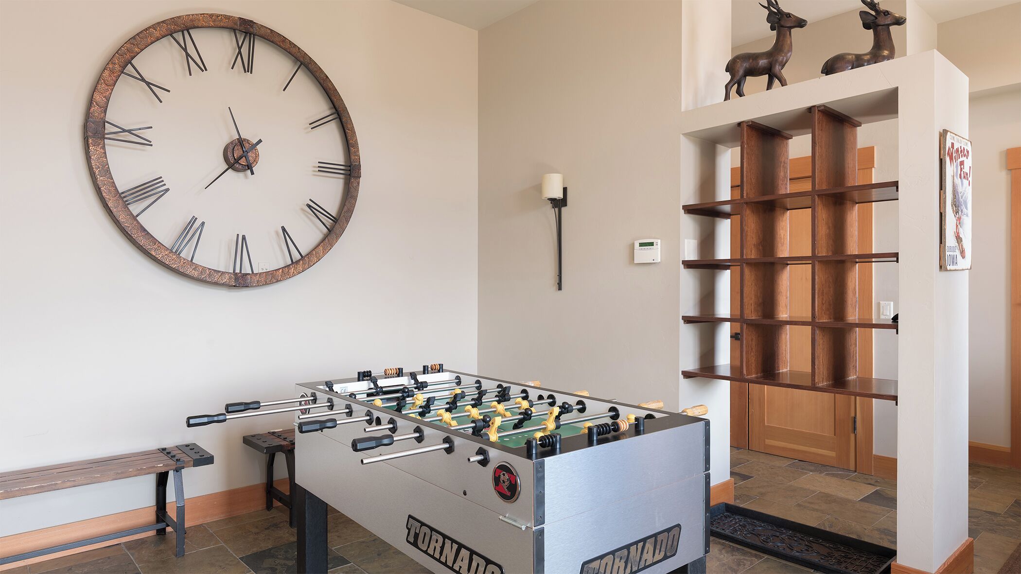 Une pièce avec une table de baby-foot, une grande horloge murale et une étagère en bois.