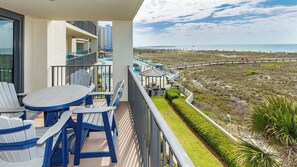 A balcony with a table and chairs, overlooking a beach and a boardwalk with beach umbrellas.