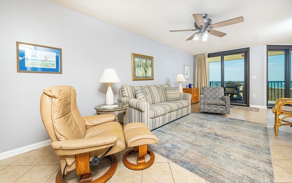 A living room with a sofa, a chair, a table, and a ceiling fan.