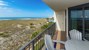 A balcony with a view of the beach and ocean, a door, and two Adirondack chairs.
