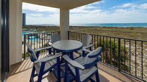 A balcony with a table and chairs, overlooking a beach and a pool.