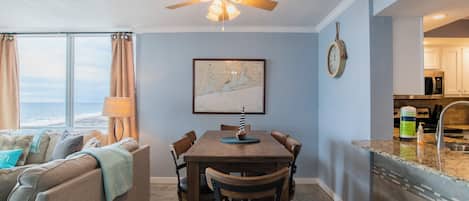 A dining area with a wooden table and chairs, a ceiling fan, a map on the wall, and a view of the kitchen.