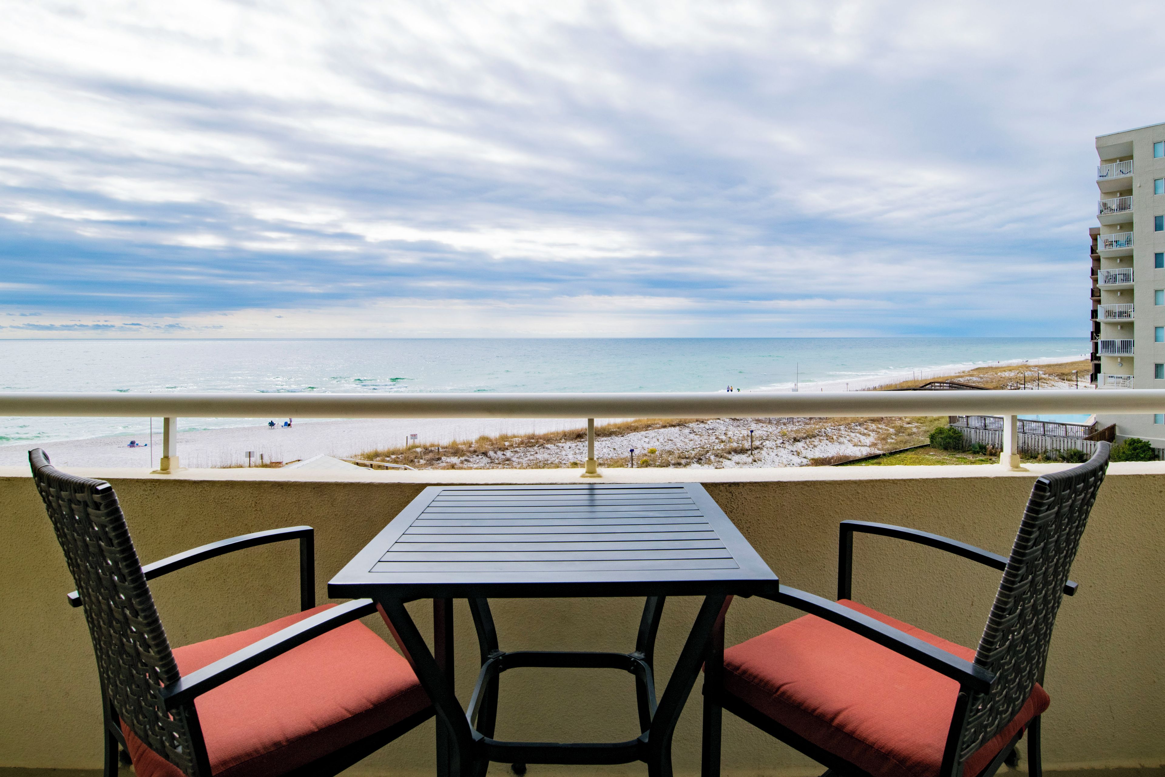 A balcony with a table and chairs overlooking a beach.