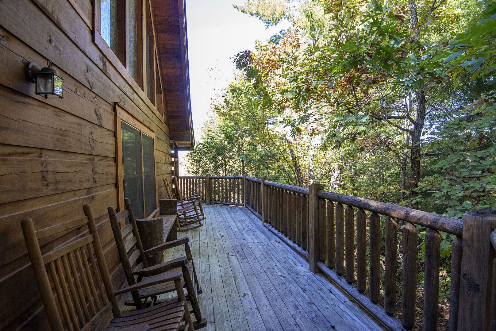 Une terrasse en bois avec des fauteuils à bascule, une clôture en bois et une vue sur les arbres.