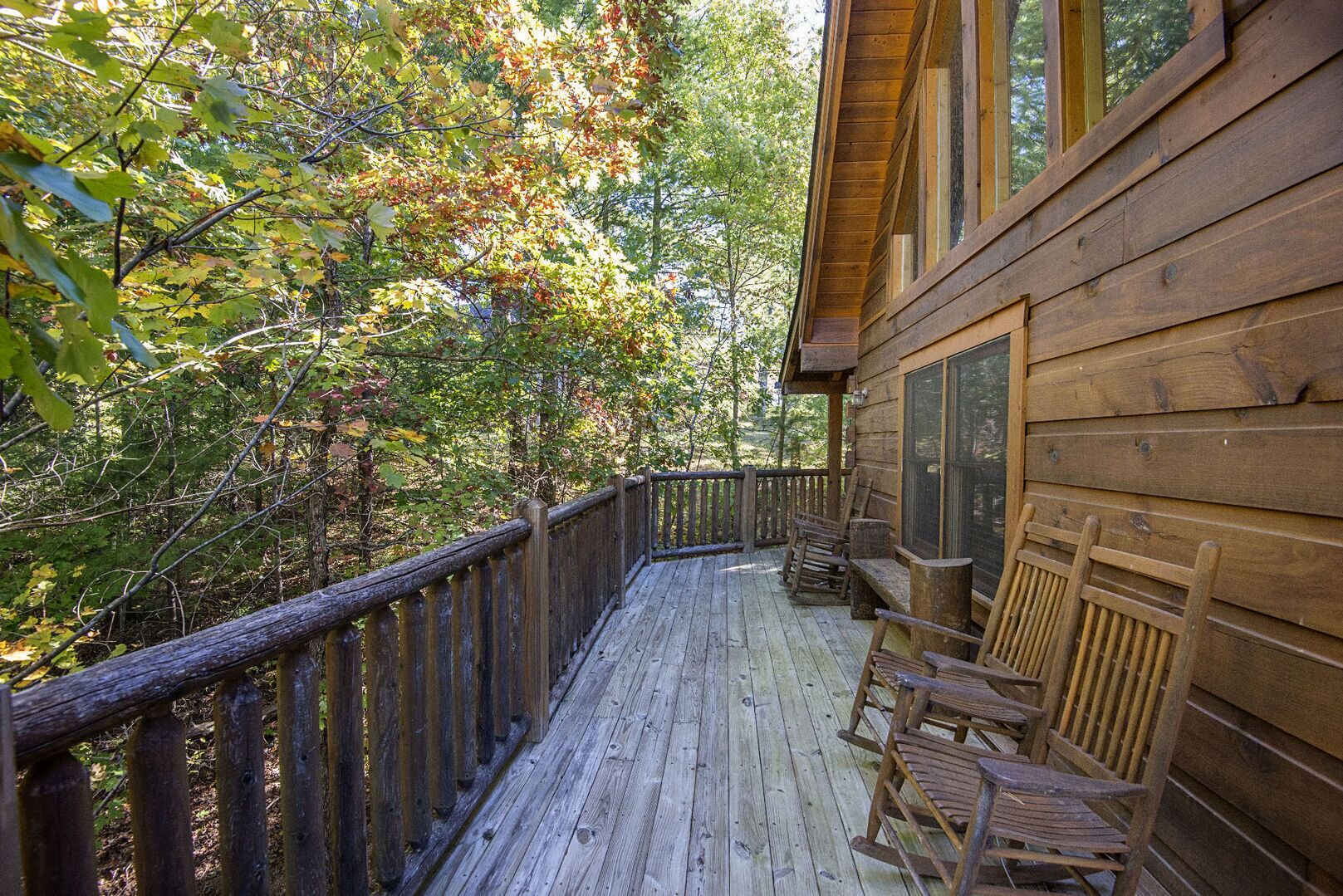 A wooden deck with a railing, surrounded by trees with autumn foliage.