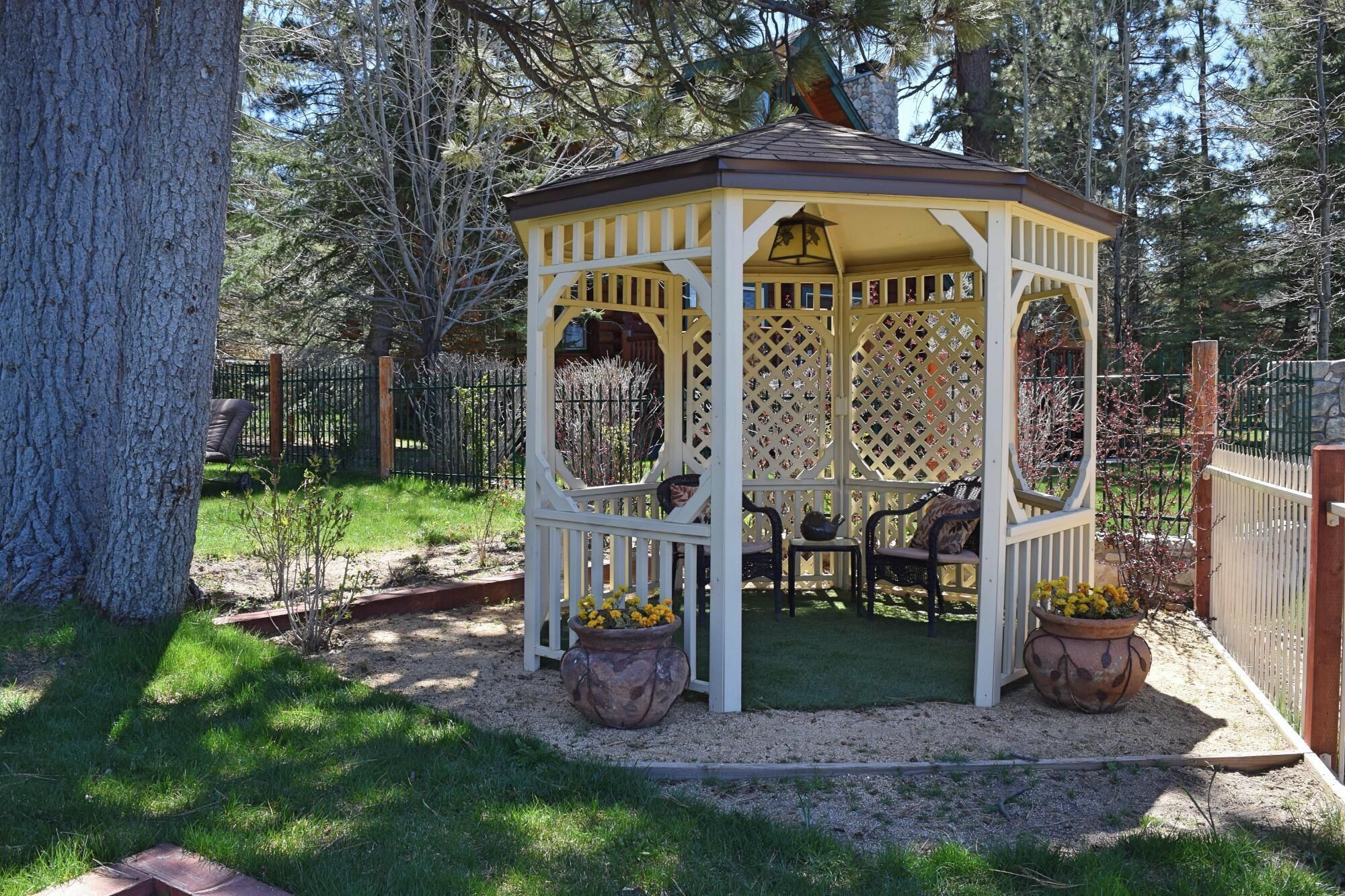 A gazebo with a lattice design, surrounded by a gravel area and potted plants.