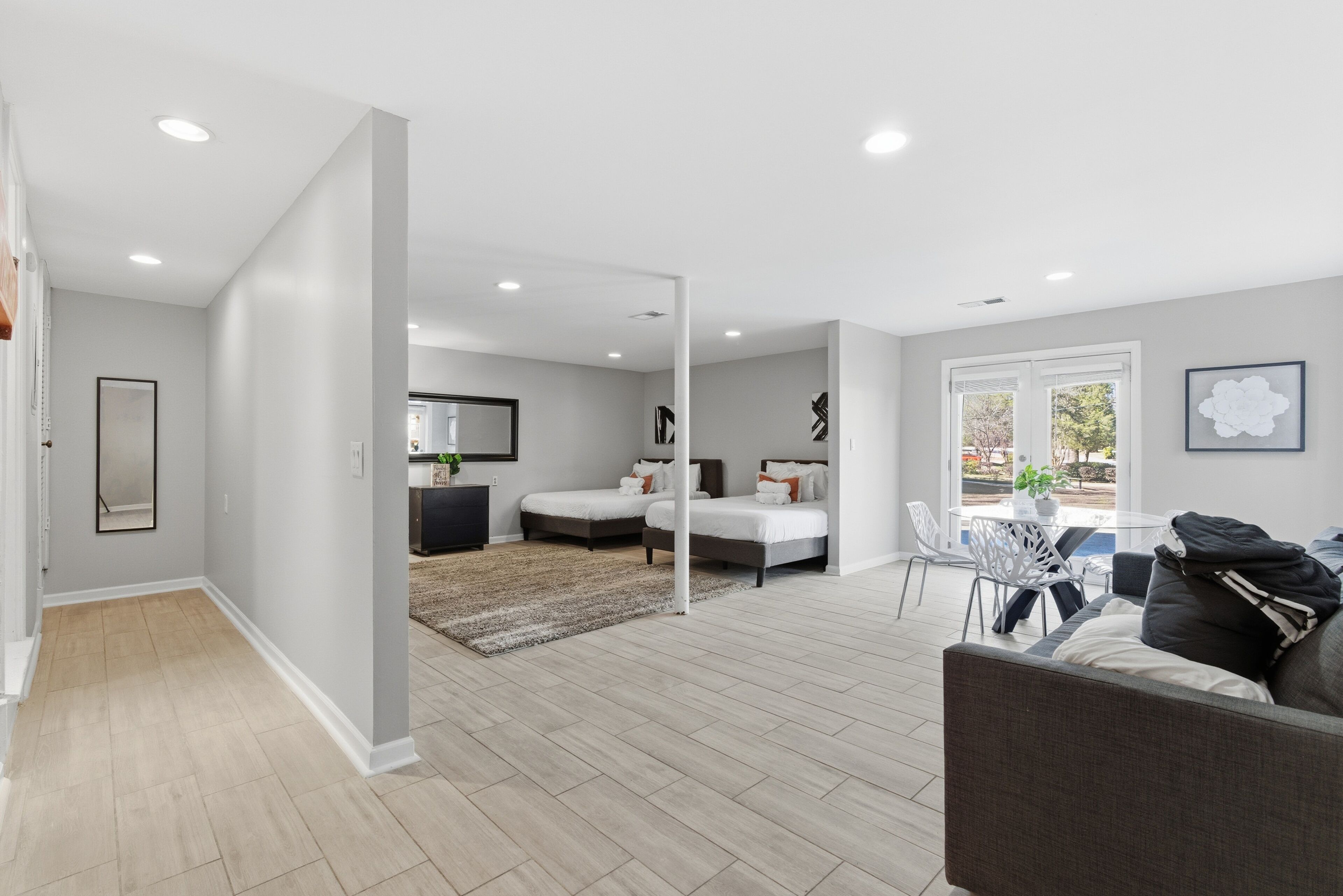 A modern living room with a sofa, a dining table, and two beds with a large window.