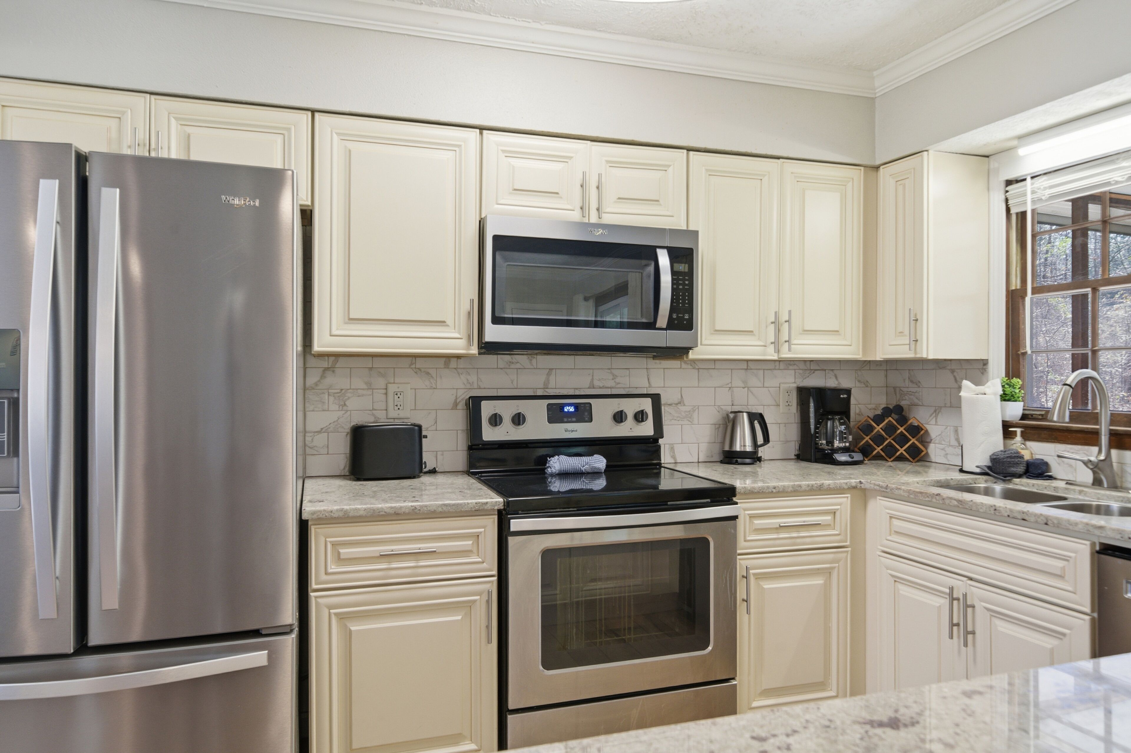 A modern kitchen with stainless steel appliances, white cabinetry, and a marble countertop.