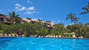 A swimming pool with lounge chairs and palm trees, surrounded by hotel buildings.