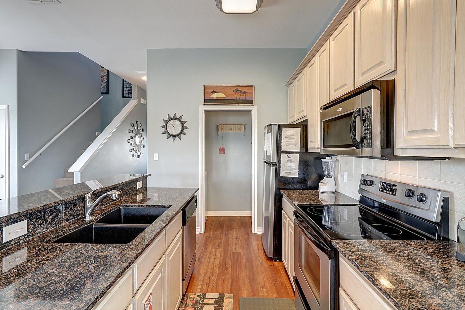 A kitchen with granite countertops, stainless steel appliances, and a wooden floor.