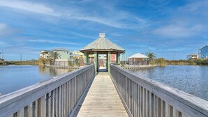 A wooden pier leading to a gazebo with a metal roof, surrounded by calm water and houses.