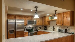 Une cuisine moderne dotée d’appareils électroménagers en acier inoxydable, de meubles en bois et de luminaires suspendus.