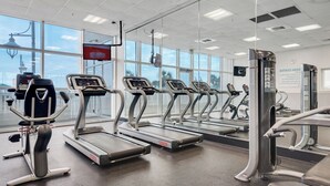 Une salle de sport équipée de tapis de course, d’appareils de musculation et dotée d’une grande fenêtre offrant une vue sur la ville.