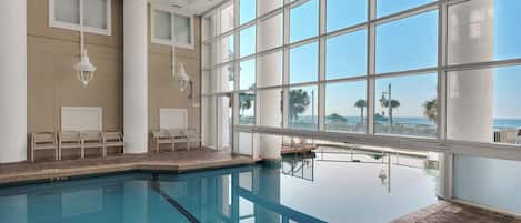 An indoor swimming pool with clear glass walls, a tiled floor, and a view of the ocean.