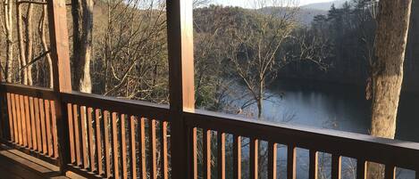 Une terrasse en bois, dotée d’une balustrade, qui offre une vue sur un lac entouré d’arbres.