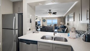 A modern kitchen with stainless steel appliances, a dishwasher, and a large window overlooking the ocean. - 🌴 Islander #507 – Fresh, Stylish & Ready for Beach Fun! 🌊✨ (Destin)