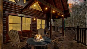 Eine Blockhütte mit einem Feuerkorb in der Mitte, umgeben von Adirondack-Stühlen.